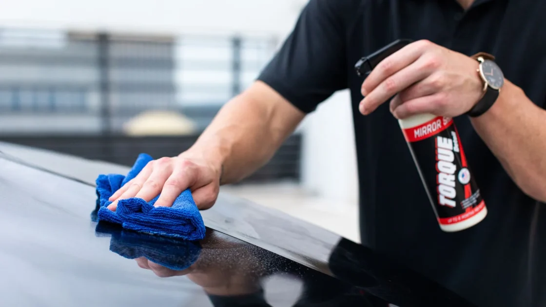 Hand using a microfiber cloth to gently clean the forward camera area on the inside of a car windshield.