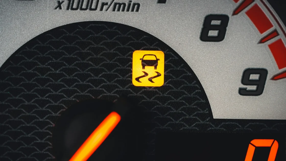 A close-up of a car dashboard showing a driver-assist warning icon glowing amber.