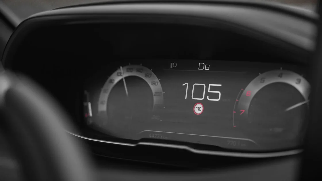 A car dashboard showing a recognized speed limit sign icon next to the speedometer while driving on a highway.