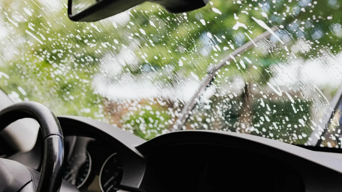 Water spraying over a car's windshield and front bumper inside an automatic car wash.
