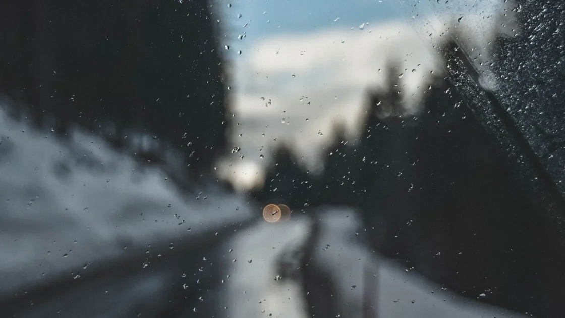 A car windshield with snow packed around the base of the interior camera on a cold morning.