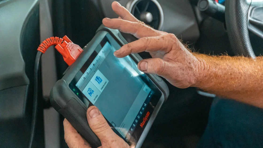 A handheld OBD-II scan tool plugged into a car's diagnostic port under the dashboard.