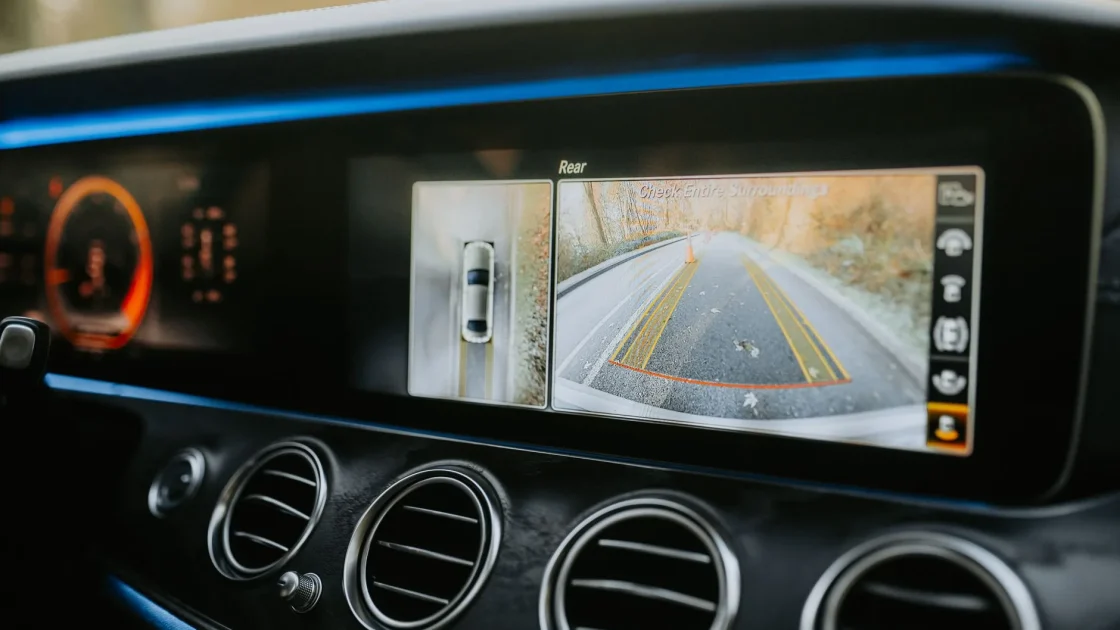 A car's dashboard display showing a rear backup camera view with parking guideline lines.