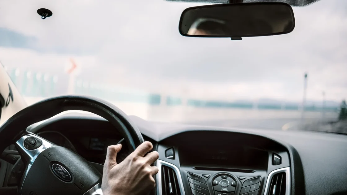 A driver's hands resting lightly on the wheel while a car travels a multi-lane highway with lane centering engaged.