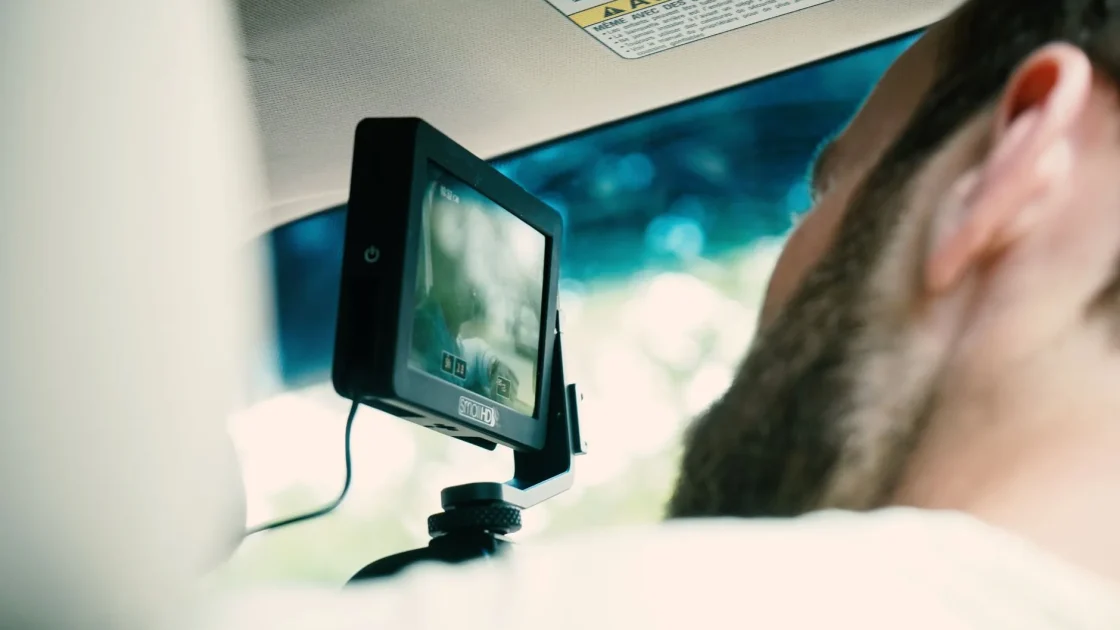 An aftermarket driver-assist camera and display mounted on the dashboard of an older car interior.