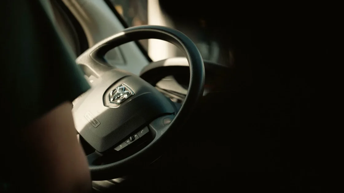A small infrared driver-monitoring camera mounted on the steering column watching a driver's face for signs of drowsiness or distraction.