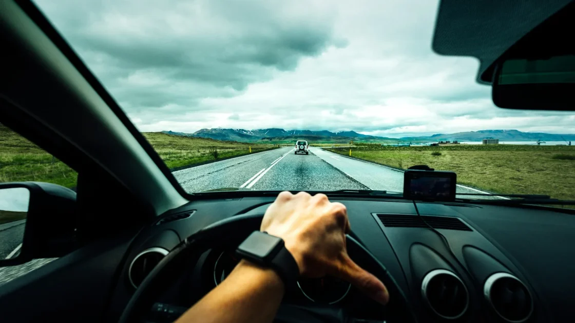 A driver's hands resting on a car steering wheel with an adaptive cruise and lane centering display lit on the dashboard.
