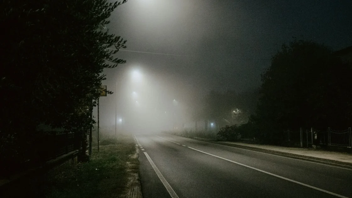 A car driving on a dark rural road at night with its high beams on, using camera-based automatic high beam assist to dim for oncoming traffic.
