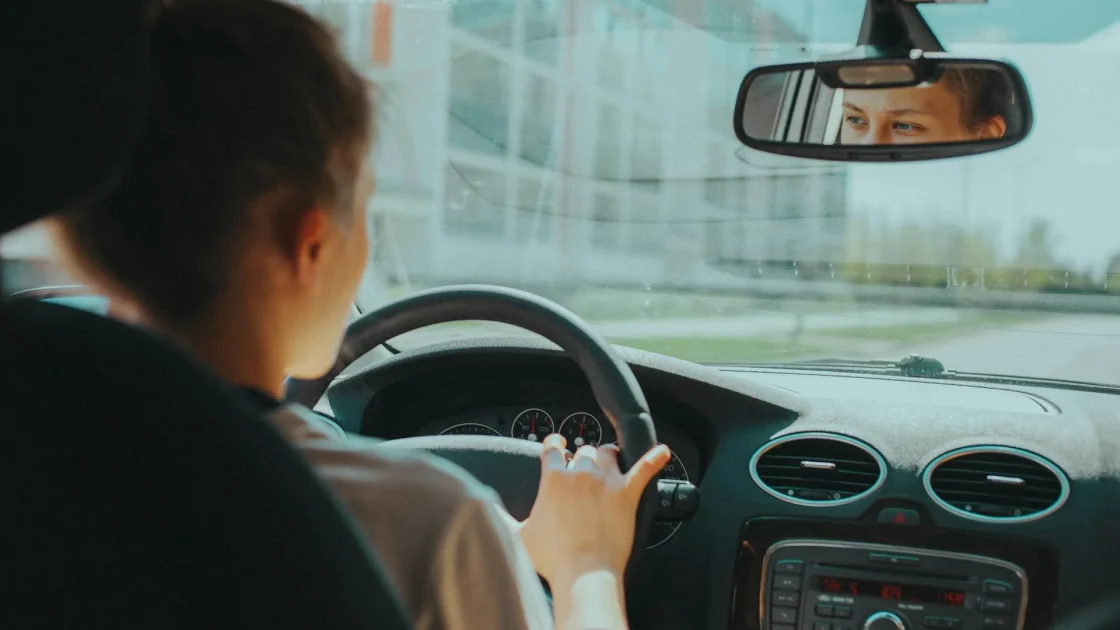 Driver's hands on a steering wheel with a lane keep assist button and highway lane markings ahead.