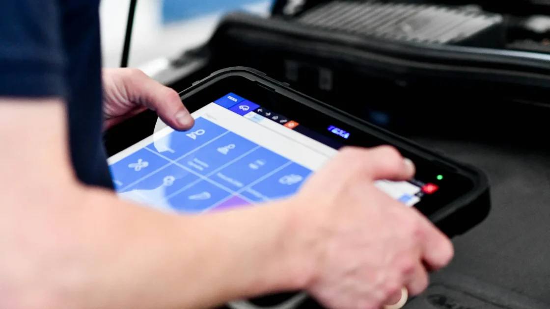 A technician holding a diagnostic scan tool connected to a car during an ADAS calibration.