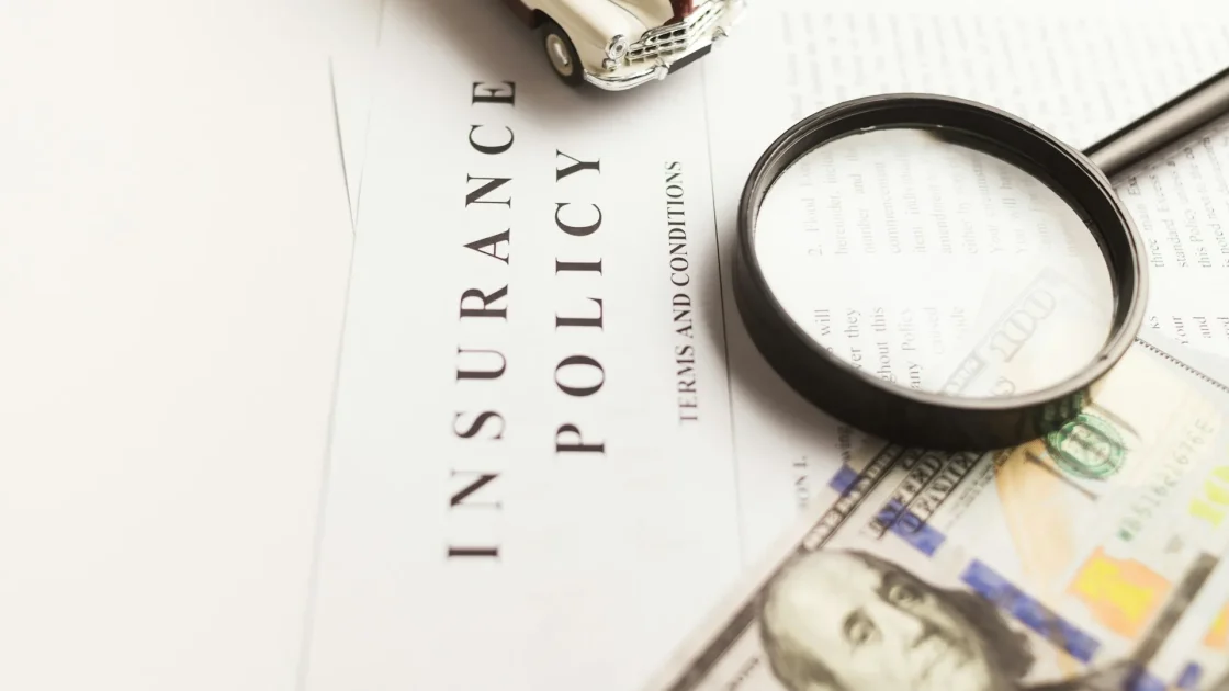 A driver reviewing an auto insurance policy document on a clipboard beside a car steering wheel.