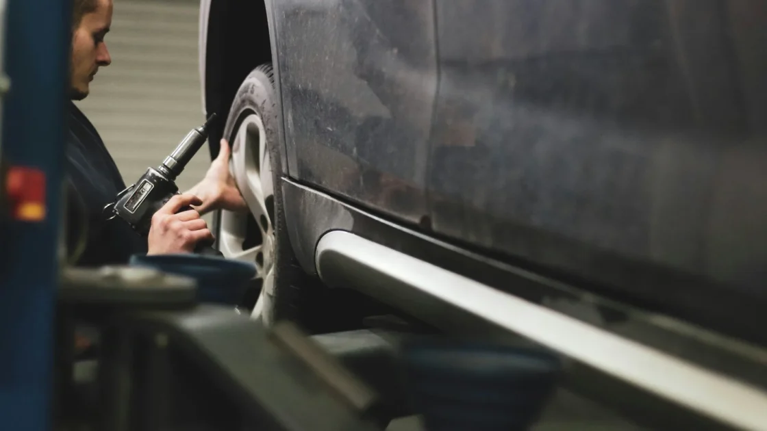 A used-car buyer crouching to inspect the front bumper and radar area of a vehicle for signs of repair.