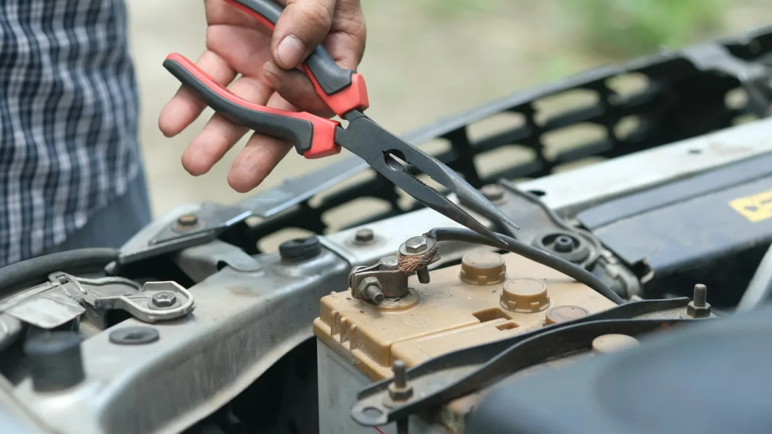 A hand loosening the negative terminal on a car's 12-volt battery with a wrench in an engine bay.