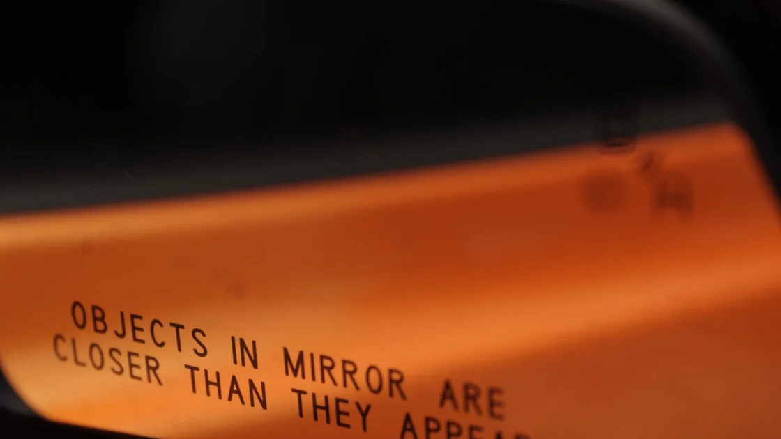A car side mirror with an illuminated amber blind spot warning indicator in the corner of the glass.