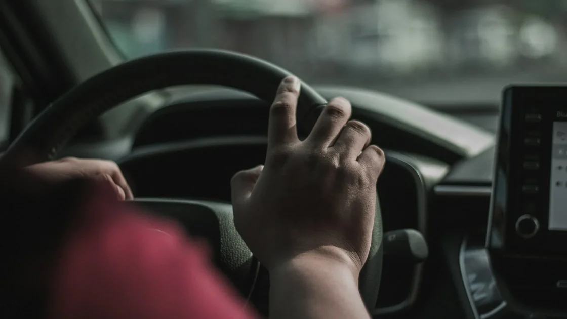 A driver's hands hovering just above a steering wheel while adaptive cruise and lane centering are active on a highway.