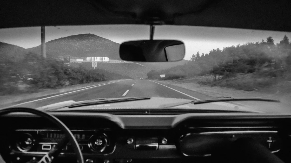 Driver's hands resting lightly on the steering wheel as a car holds its lane on a marked highway with lane assist active.