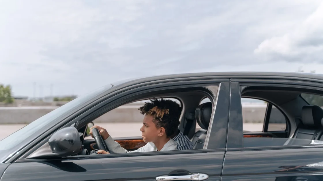 A parent in the passenger seat coaching a teenage driver whose hands are correctly placed on the steering wheel.