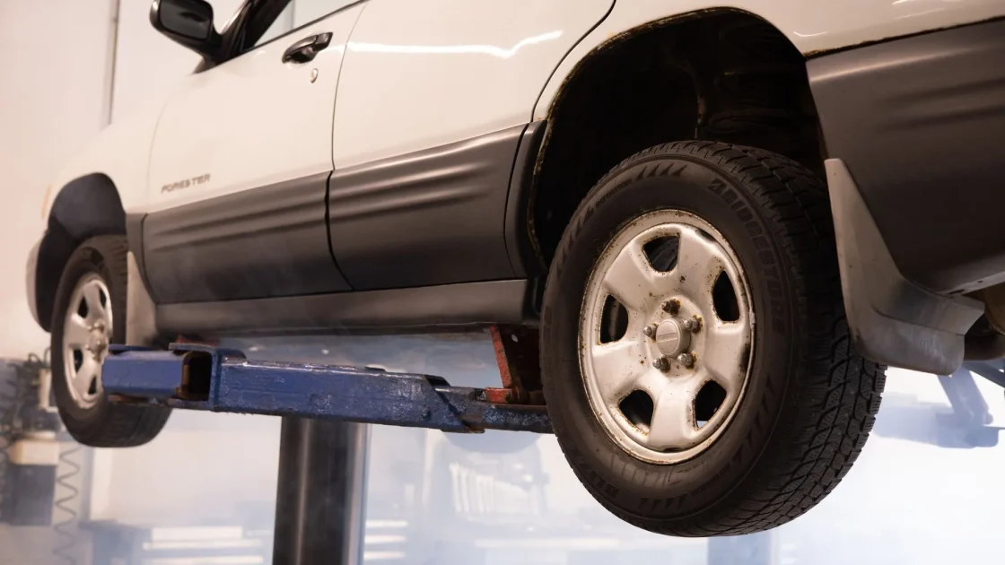 A car raised on a shop lift with a technician rotating the tires between axles.